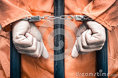 Handcuffed hands of a prisoner behind the bars of a prison Stock Photo