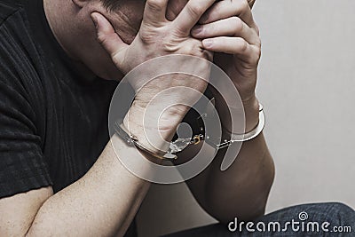 Handcuffed man covering his face with his hands. Arrested and handcuffed criminal man with handcuffs on his hands cover his head Stock Photo