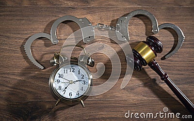 Handcuffs, judge gavel and alarm clock on the wooden background Stock Photo