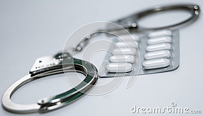 Handcuffs and pills and drugs on white table. Stock Photo