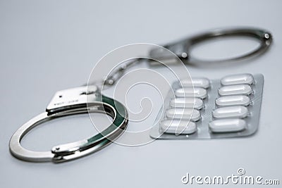 Handcuffs and pills and drugs on white table. Stock Photo