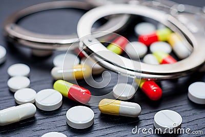 Handcuffs and pills and drugs on wooden table Stock Photo