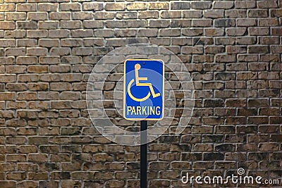 Handicap parking sign against a stone brick wall illuminated by sunlight Stock Photo