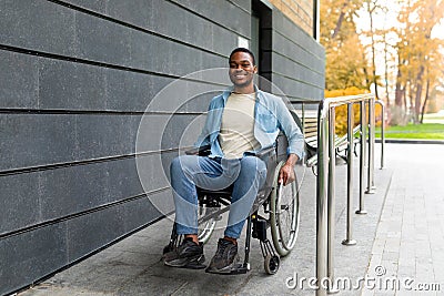 Handicapped accessible city. Positive impaired Afro man in wheelchair leaving building on ramp outdoors in autumn Stock Photo