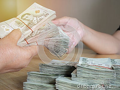 Handing over stacks of Thai banknote to other hand with soft light background Stock Photo