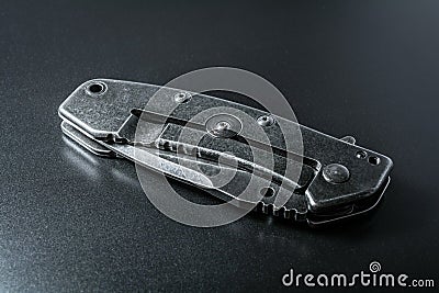 Handle Of A Closed Black Folding Knife Lying On Dark Ground With Reflection Stock Photo