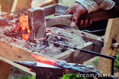 Handmade blacksmith at the forge on the outdoor. Hammer blows on the iron disc on the anvil. Forging sword blades retro weapons Stock Photo