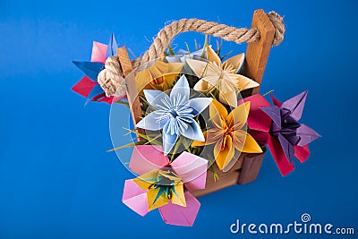 Handmade colored paper flowers origami bouquet paper craft art in a basket with grass in the studio on colored blue Stock Photo