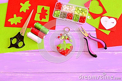 Handmade keychain for handbag or backpack. Strawberry keychain made of felt and beads. Craft tools and materials on wood table Stock Photo