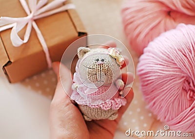 Handmade knitted toy. Knitted cat in a pink dress and bow in female hand on a background of gift box. Birthday gift idea Stock Photo