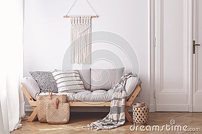 Handmade wicker bags on herringbone parquet floor of a warm living room interior with an artisan, beige macrame on a white wall Stock Photo