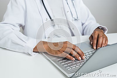 Hands of an afro doctor using a laptop on the top of a white desk Stock Photo