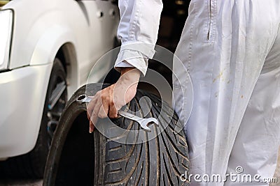 Hands of automotive mechanic in uniform with tire and wrench for fixing car at the repair garage background. Stock Photo