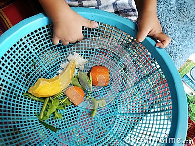 Hands of the baby playing with piece of vegetable in the blue basket in the kitchen with parents Family House Bangkok Thailand Stock Photo
