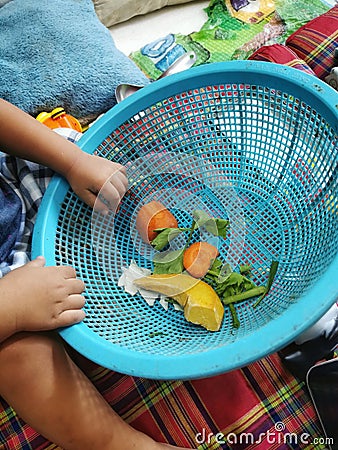 Hands of the baby playing with piece of vegetable in the blue basket in the kitchen with parents Family House Bangkok Thailand Stock Photo