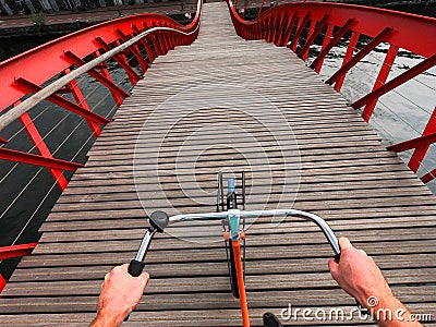 Hands on a Bicycle handlebar POV view. Orange bike on the wooden red Python bridge in Amsterdam, Netherlands Editorial Stock Photo