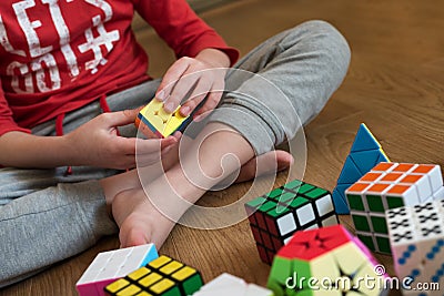 Hands of boy trying to solve the puzzle against various pyramid and cube toy puzzles background. Solving difficult tasks or stay Editorial Stock Photo