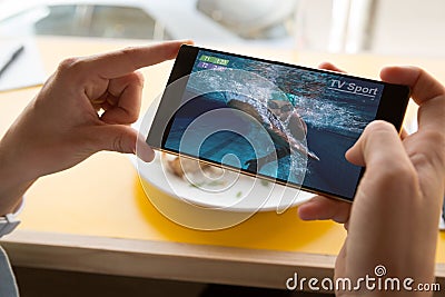 Hands of caucasian man at restaurant watching swimming competition on smartphone Stock Photo