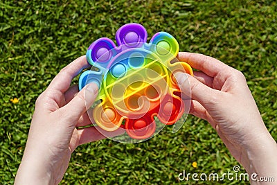 Hands press rubber pimples of pimpled anti stress pop it toy on green lawn Stock Photo