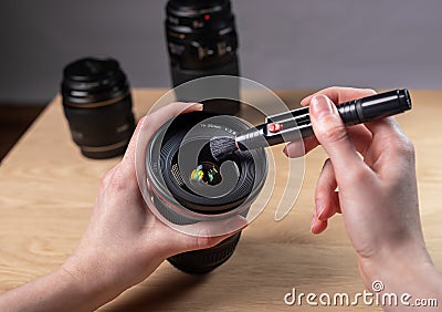 Hands closeup cleaning digital camera lens with professional brush tool, removing dust Stock Photo