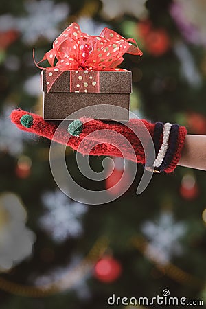 Hands in colorful red gloves holding give box with beautiful bow Stock Photo