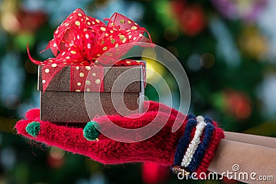 Hands in colorful red gloves holding give box with beautiful bow Stock Photo