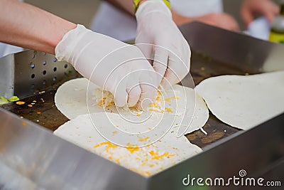 Hands of cook in latex gloves Sprinkling with cheese tortillas for preparing fresh fajita. Concept of national food Stock Photo