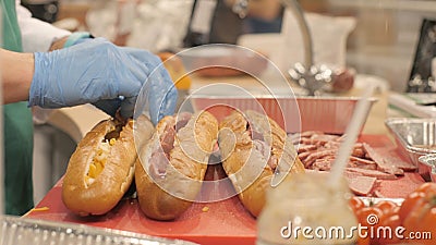 Hands cook putting pieces sausage in cut up baguette in fast food cafe Stock Photo