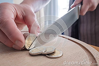 Hands cut euro coins with a knife, separating them like pieces of food, on a cutting board. Concept of taxes, fraud or Stock Photo