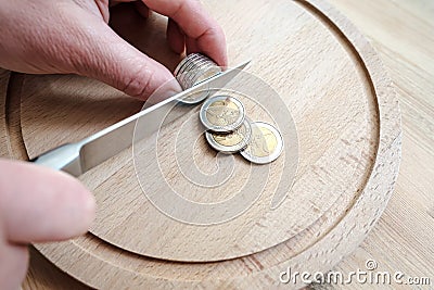 Hands cut euro coins with a knife, separating them like pieces of food. Concept of taxes, fraud or profit. Top view. Stock Photo
