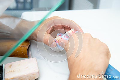 The hands of a dental technician are working on an artificial tooth using a dental instrument, a drill. Stock Photo