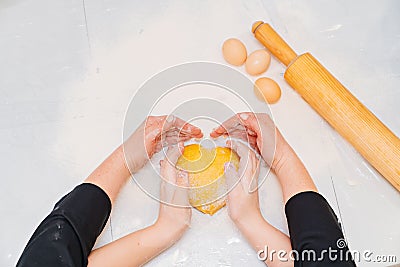 hands with dough in the shape of a heart, flour and eggs on the table. Stock Photo