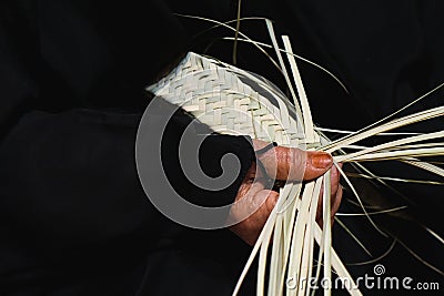 Hands of elderly arab woman artisan in traditional black dress close up weaving basket from dried organic palm leaves. Stock Photo