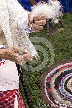 Hands of an elderly woman who weaves wool thread using a spindle Stock Photo