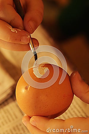 Hands of five years old girl painting yellow heart on blowed easter egg with thin brush Stock Photo