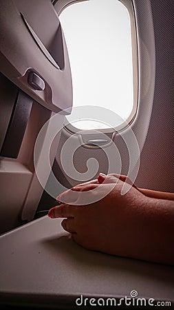 Hands on the folding table of the chair in the cabin of the aircraft near the porthole Stock Photo