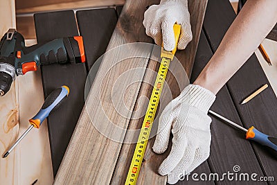 Hands in gloves of joiner in carpentry. Carpenter is measuring length of wood planks or timbers by measuring tape or ruler. Stock Photo