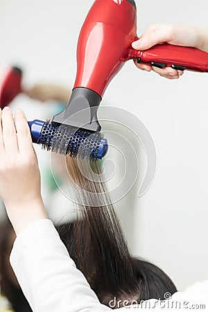 Hands of hairstylist drying brunette hair of client using red hairdryer and blue comb in professional beauty salon Stock Photo