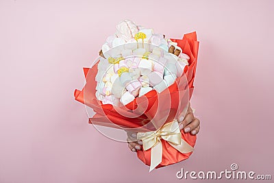 Hands hold edible marshmallow bouquet through torn hole on pink paper background. Bakery advertising concept, recipe Stock Photo