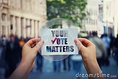 Hands hold a paper sheet with the message your vote matters over a crowded street background. People legal and democratic rights, Stock Photo