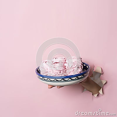 Hands hold a plate with homemade pink marshmallows through a torn hole on a pink paper background. Bakery advertising concept, rec Stock Photo