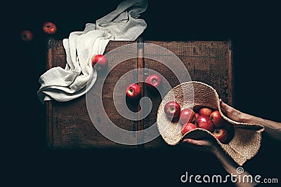 Hands holding apples in straw hat in dark background Stock Photo