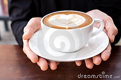 Hands holding cup of hot coffee latte with heart shaped foam art Stock Photo