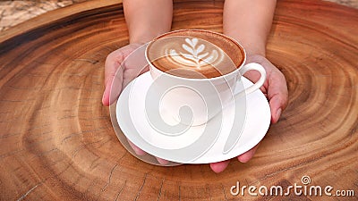 Hands holding a cup of hot latte cappuccino coffee on wooden table Stock Photo