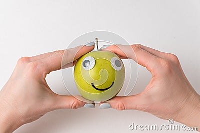 Hands holding cute little Apple with Googly eyes and drawn smile. Apple haracter on white background Stock Photo