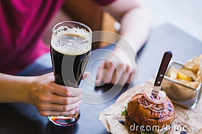 Hands holding glass of cold dark beer. Burgers with french fries on the table Stock Photo
