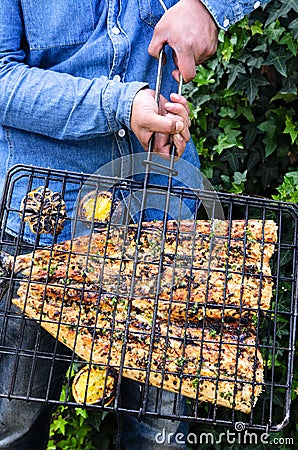 Hands holding a grill containing a barbequed fish Stock Photo