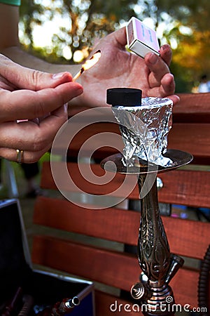 Hands holding matches and burning coal for hookah in the park Stock Photo