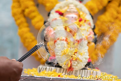 Hands Holding or offering incense or agarbatti stick in front of lord vinayaka or Ganesha while praying or worshiping Stock Photo