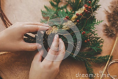 Hands holding pine cones, berries, fir branches, thread, scissors on wooden table. Authentic rural wreath. Christmas wreath Stock Photo